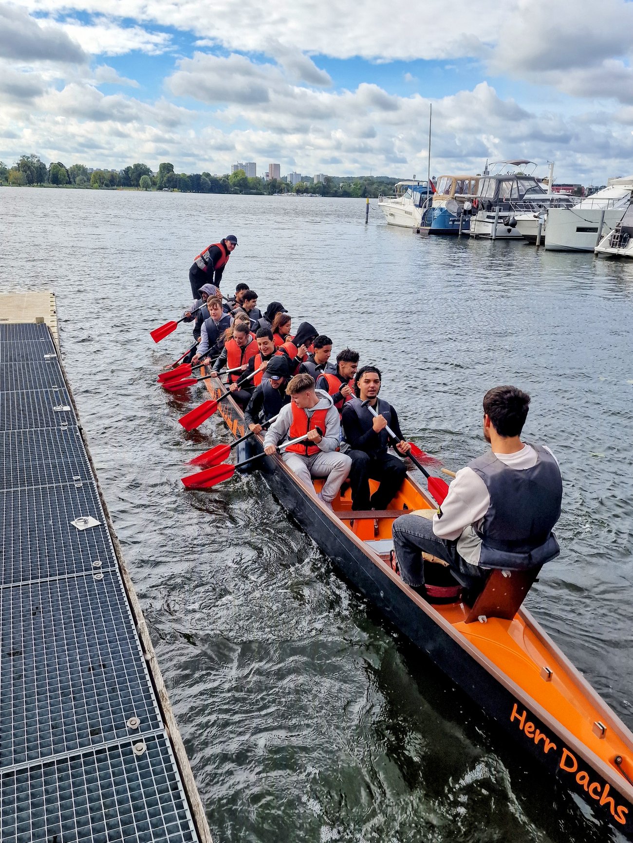 Schüler sitzen in einem Drachenboot, dass neben einem Steg schwimmt