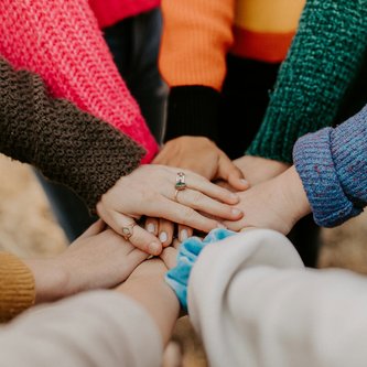 Gruppe stapelt Hände als Symbol für Gemeinschaft und Zusammenhalt
