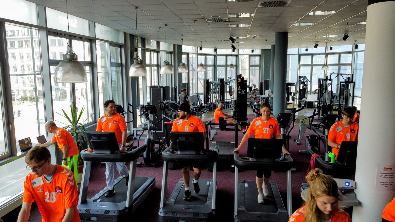 Teilnehmer in orangen Trikots auf Laufbändern