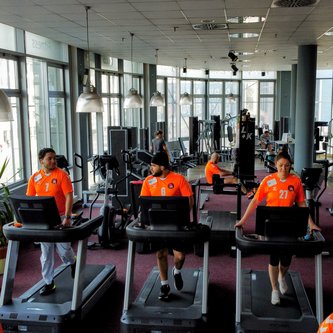 Teilnehmer in orangen Trikots auf Laufbändern