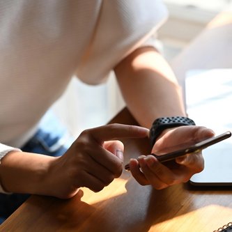 Schüler hält Smartphone und sitzt vor Laptop