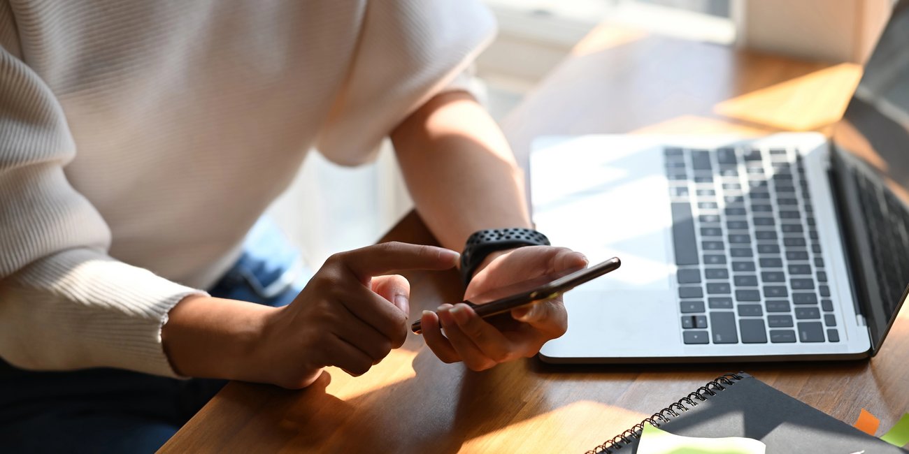 Schüler hält Smartphone und sitzt vor Laptop