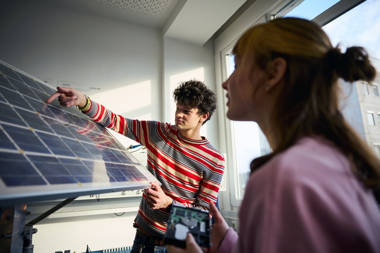 Junger Mann zeigt auf ein Solarpanel