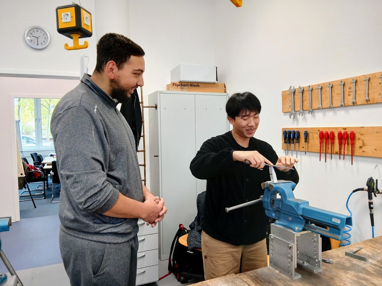 koreanischer Schüler lacht an Werkbank, deutscher Schüler steht daneben