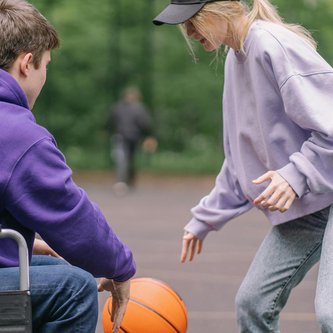 Frau spielt Ball mit Mann im Rollstuhl