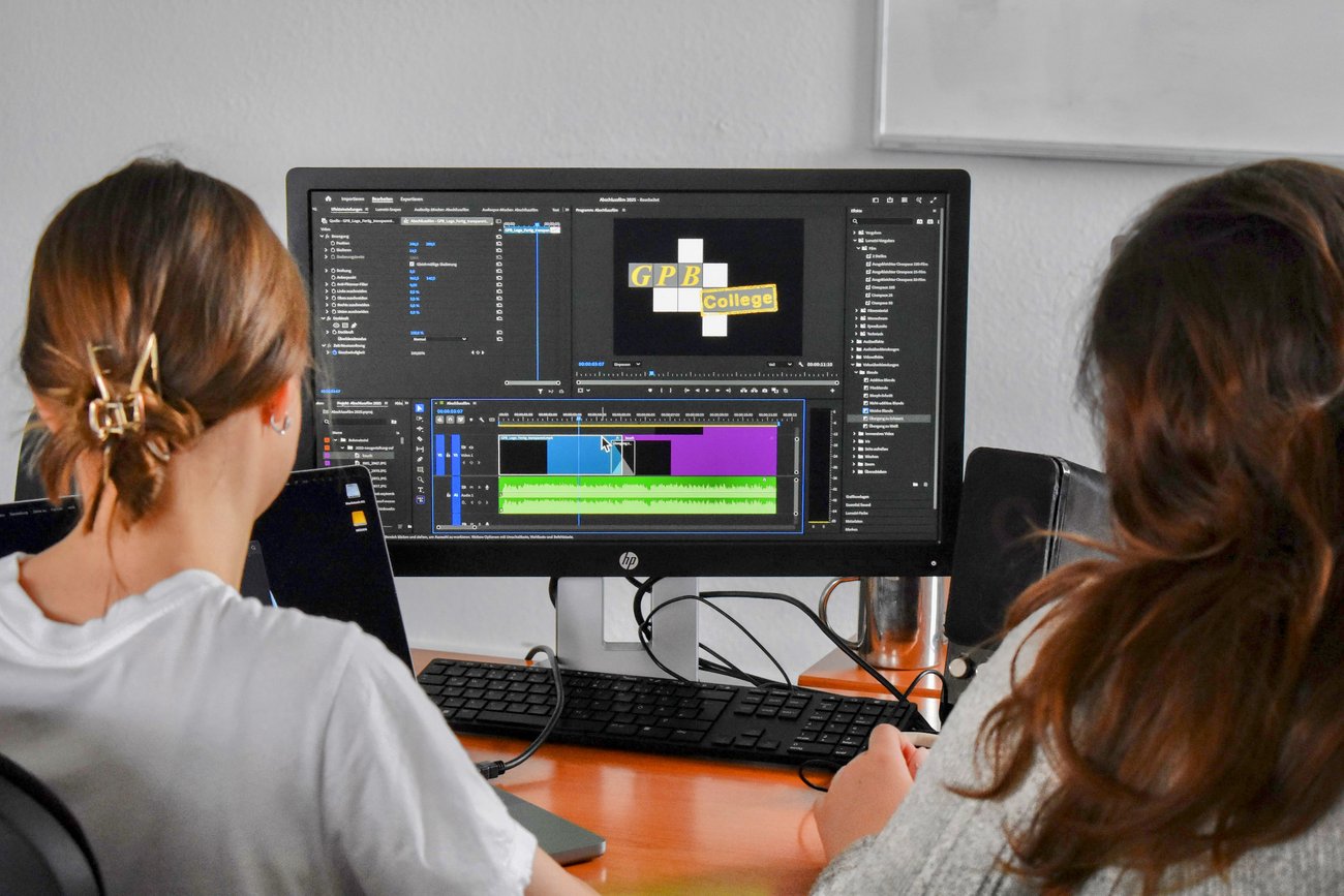 zwei Schülerinnen von hinten vor einem PC-Bildschirm mit dem Logo vom GPB College