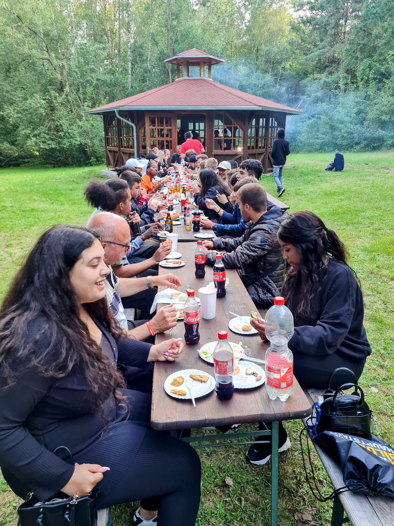Schüler sitzen an einer langen Tafel im Freien mit Essen und Getränken