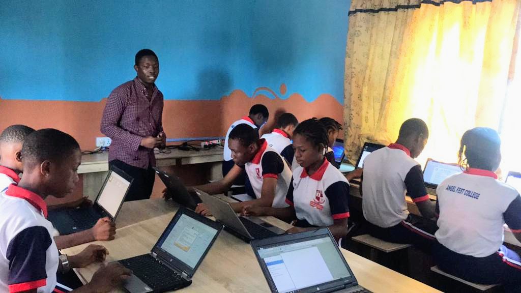 Lehrer steht und spricht zu afrikanischen Schülern, die vor Laptops sitzen