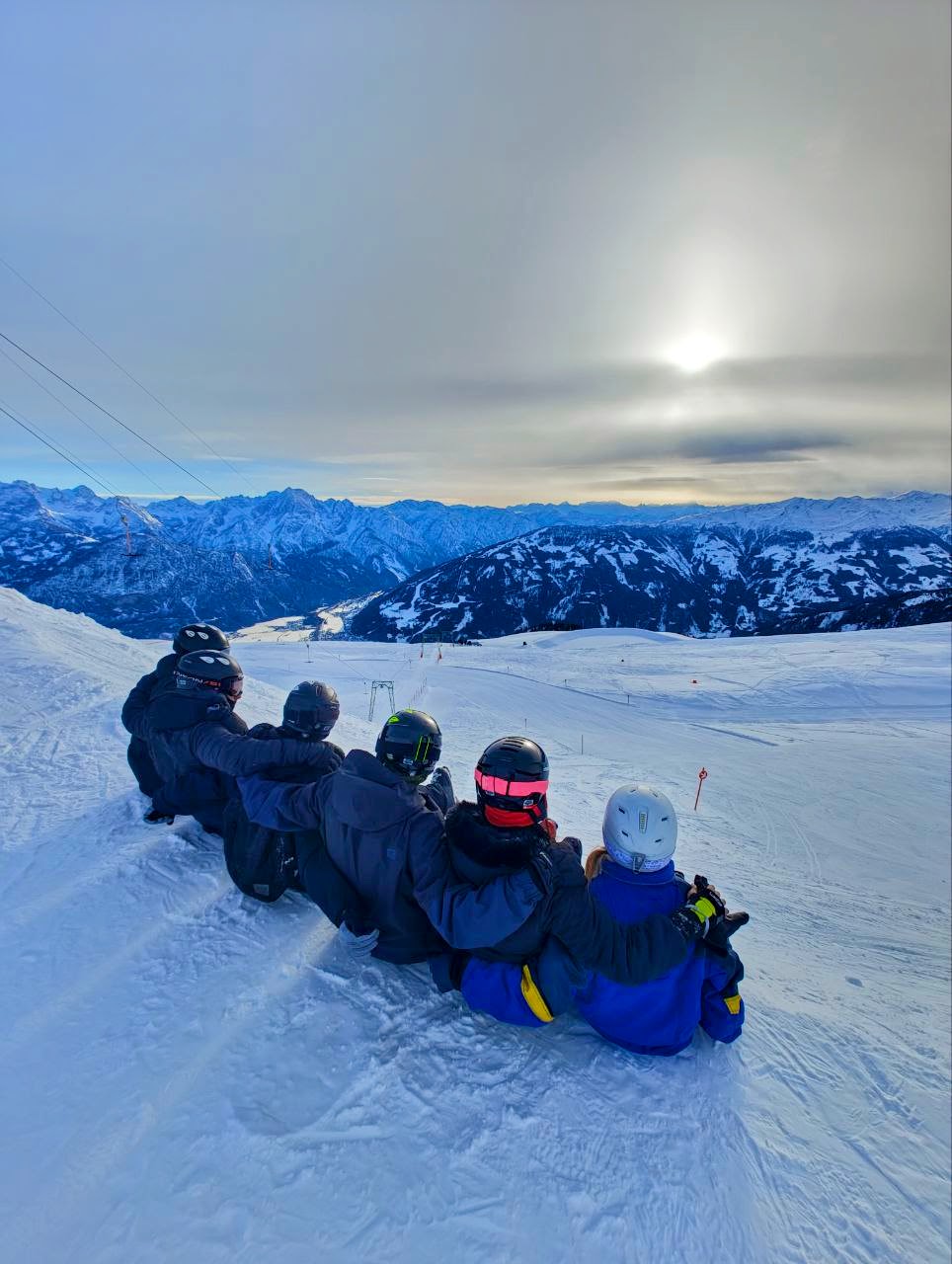 Gruppe sitzt im Schnee mit Sonne im Hintergrund