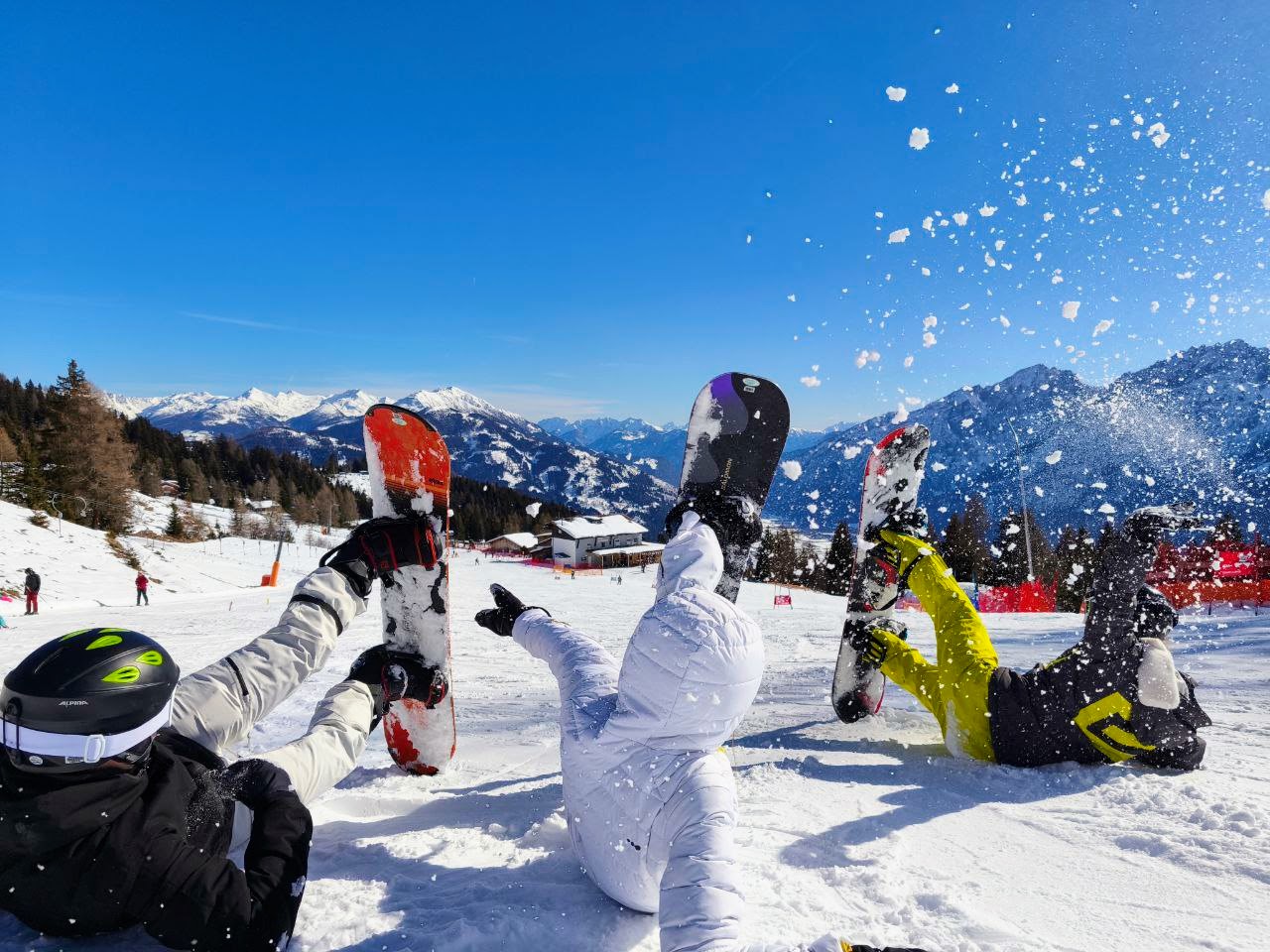 Drei Snowboarder liegen und wirbeln Schnee auf