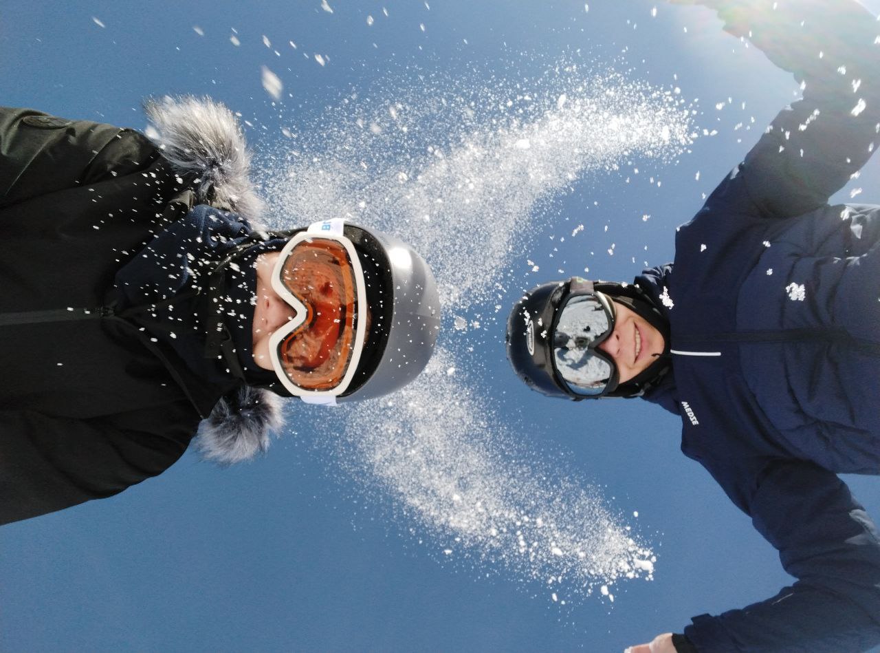 zwei Köpfe mit Skibrille und Helm und in die Höhe geworfener Schnee